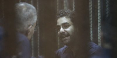 Egyptian activist Alaa Abdel Fattah gestures inside a defendant's cage during his new trial in Cairo, Egypt on May 23, 2015 with 24 other defendants including former Egyptian President Mohammad Morsi on trial for insulting the judiciary. Cairo Criminal court postponed on Saturday, the trial of former President, Morsi, to July 27. [Mostafa el-Shemy/Anadolu Agency/Getty Images